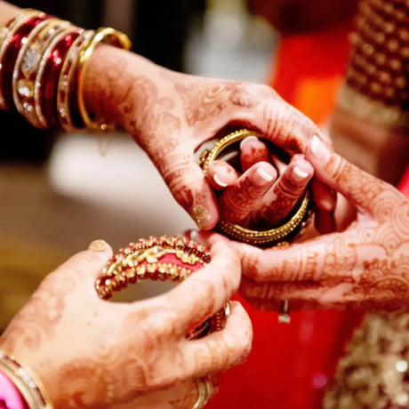 Hands delicately placing ornate gold jewelry during a Bangle Ceremony celebrating significant life transitions.