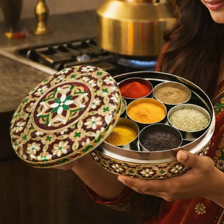 Ornate brown and gold enamel indian spice box with six compartments of colorful spices in metallic containers for masala dabba.