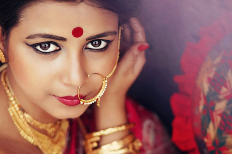 A South Asian woman in traditional attire stands elegantly, adorned with a vibrant bindi on her forehead. Her outfit features intricate embroidery and rich colo