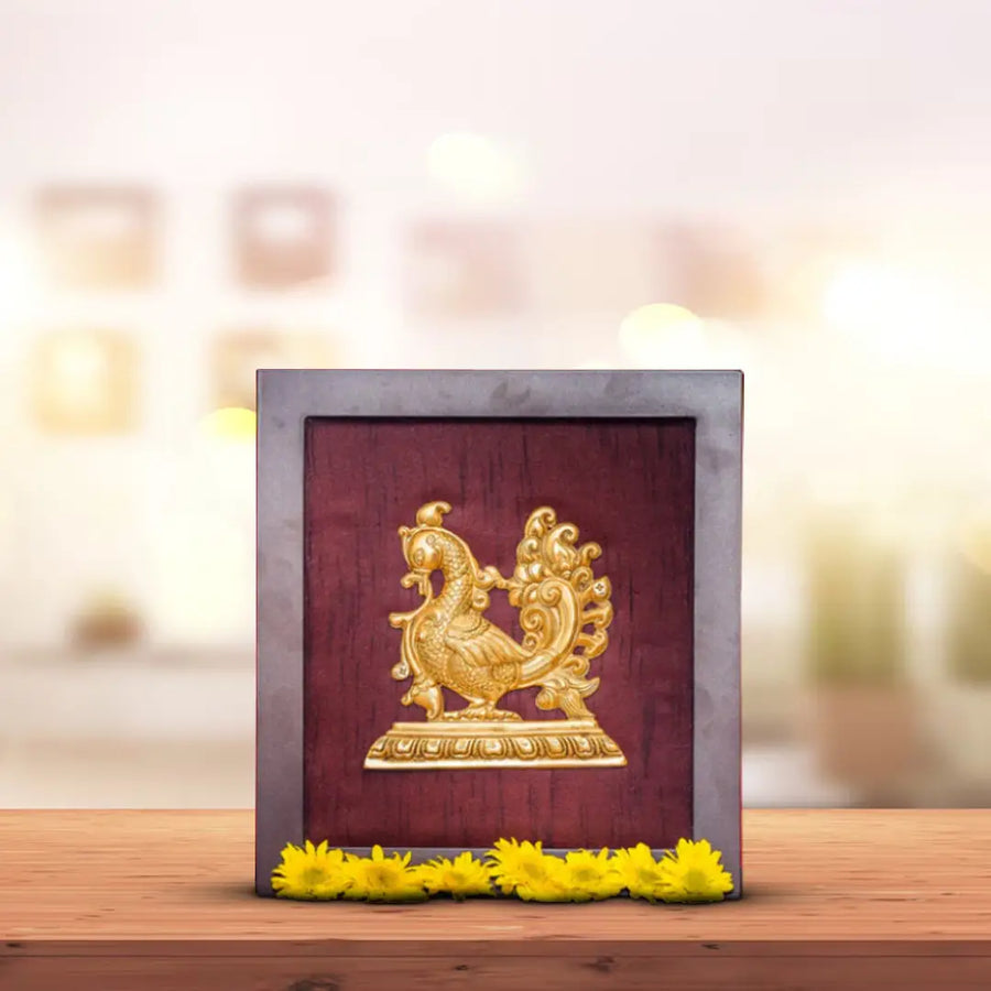 A golden peacock figurine in a framed box sits on a wooden table, decorated with yellow flowers.