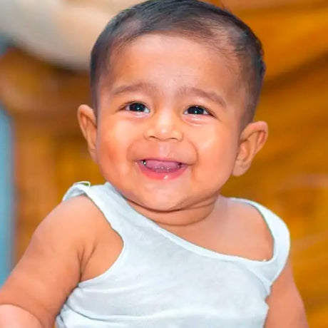 A joyful baby sits on a bed, beaming with a bright smile, radiating happiness and innocence.