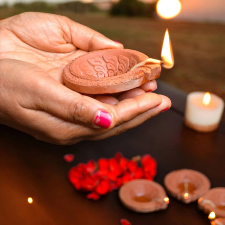 Lit clay diya with intricate patterns held in cupped hands showcasing traditional Indian craftsmanship