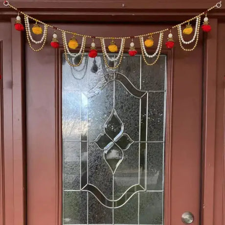 A colorful Indian toran decorated with traditional patterns hangs at a doorway, set against a cozy home interior, enhancing the welcoming atmosphere.