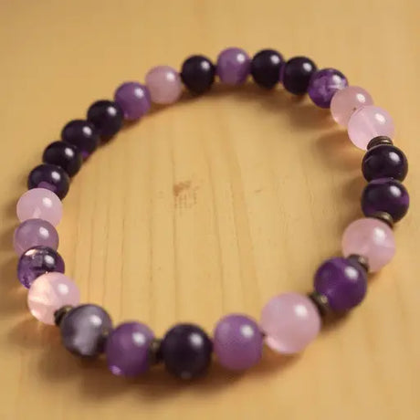Close-up of a healing stones bracelet with glowing amethyst and rose quartz beads on a wooden background, radiating calm and tranquility.