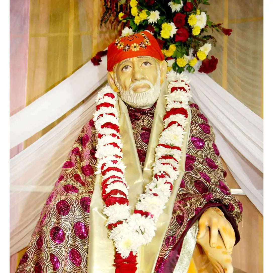 "Devotee praying before a large white Sai Baba statue in a lush garden."