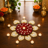 A circular lotus flower rangoli cutout made of red and white petals with gold accents surrounded by lit tea light candles on wood