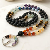 A handcrafted 108 mala beads necklace with black lava rock, tiger eye, chakra gemstones, and a silver tree of life pendant