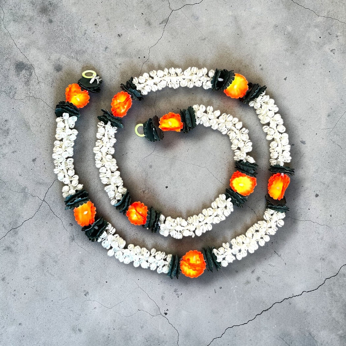 A spiral arrangement of 2 strings artificial jasmine buds garland with white blossoms black accents and orange centers for festivals