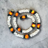 A spiral arrangement of 2 strings artificial jasmine buds garland with white blossoms black accents and orange centers for festivals