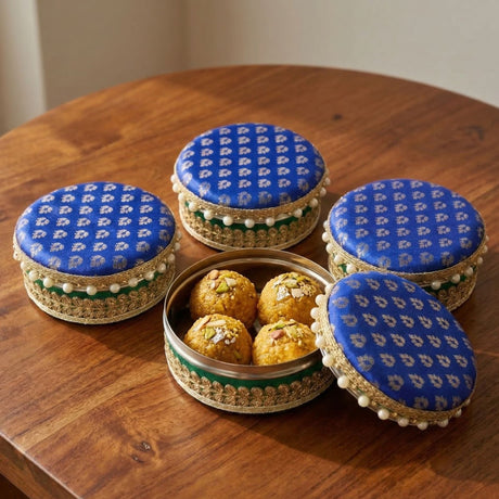 Blue patterned fabric-lidded steel ladoo boxes with gold trim and pearls, one open showing golden sweets for festive gifts