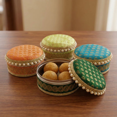 Four ornate round steel ladoo boxes in orange green and blue with embroidered lids gold trim and pearl bead accents
