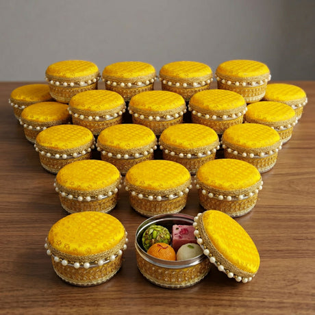 Yellow fabric covered round 4 ct steel ladoo box with gold trim and pearl embellishments for festive sweets gift