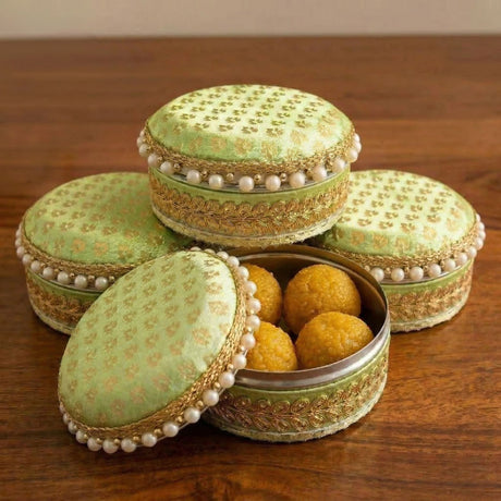 Lime green fabric covered steel ladoo box with gold embroidery and pearl trim containing golden laddoos for Diwali