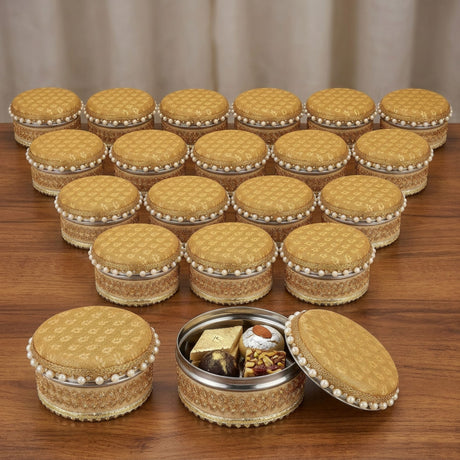 Golden fabric steel ladoo boxes with pearl trim and metallic accents for holi diwali sweets gift on wooden surface