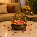 Ornate brass urli bowl with bell centerpiece in dark wood holding floating pink and yellow lotus flowers for home decor