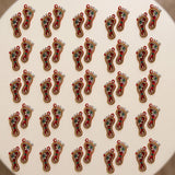 Acrylic lakshmi charan paduka feet pair in red and gold embroidery with green gemstones and white bead accents for diwali decor