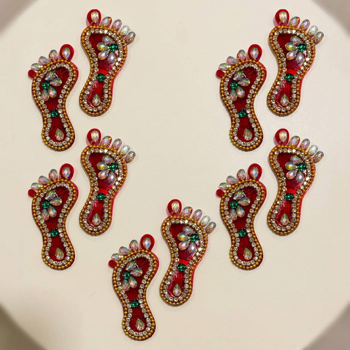 Red and gold acrylic lakshmi charan paduka feet stickers adorned with green gemstones and clear rhinestones for diwali decoration