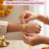A cheerful green smiley face animal theme rakhi with floral design white pearls on an orange adjustable thread for brother