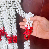 A hand holds an artificial jasmine buds and rose garland with white and red flowers for pooja and festive decor