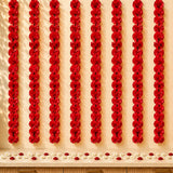 Red artificial carnation garlands hanging vertically as marigold strings for diwali and pooja decoration backdrop