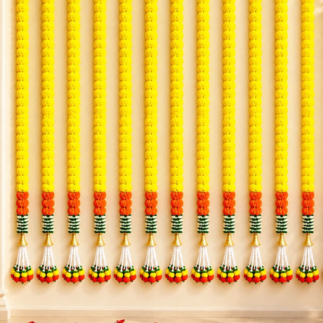 Artificial marigold garland with vibrant yellow and orange flowers, green striped accents, and gold tassels for festive decor