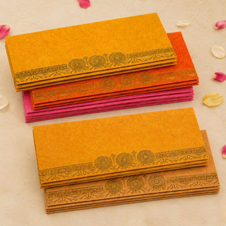 Stacks of vibrant orange and pink money envelopes with gold foil decorative wheel patterns for Indian wedding gifts