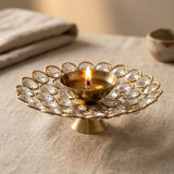 A golden brass decorative diya with crystal-encrusted acrylic glass floral design and lit candle for diwali puja decor