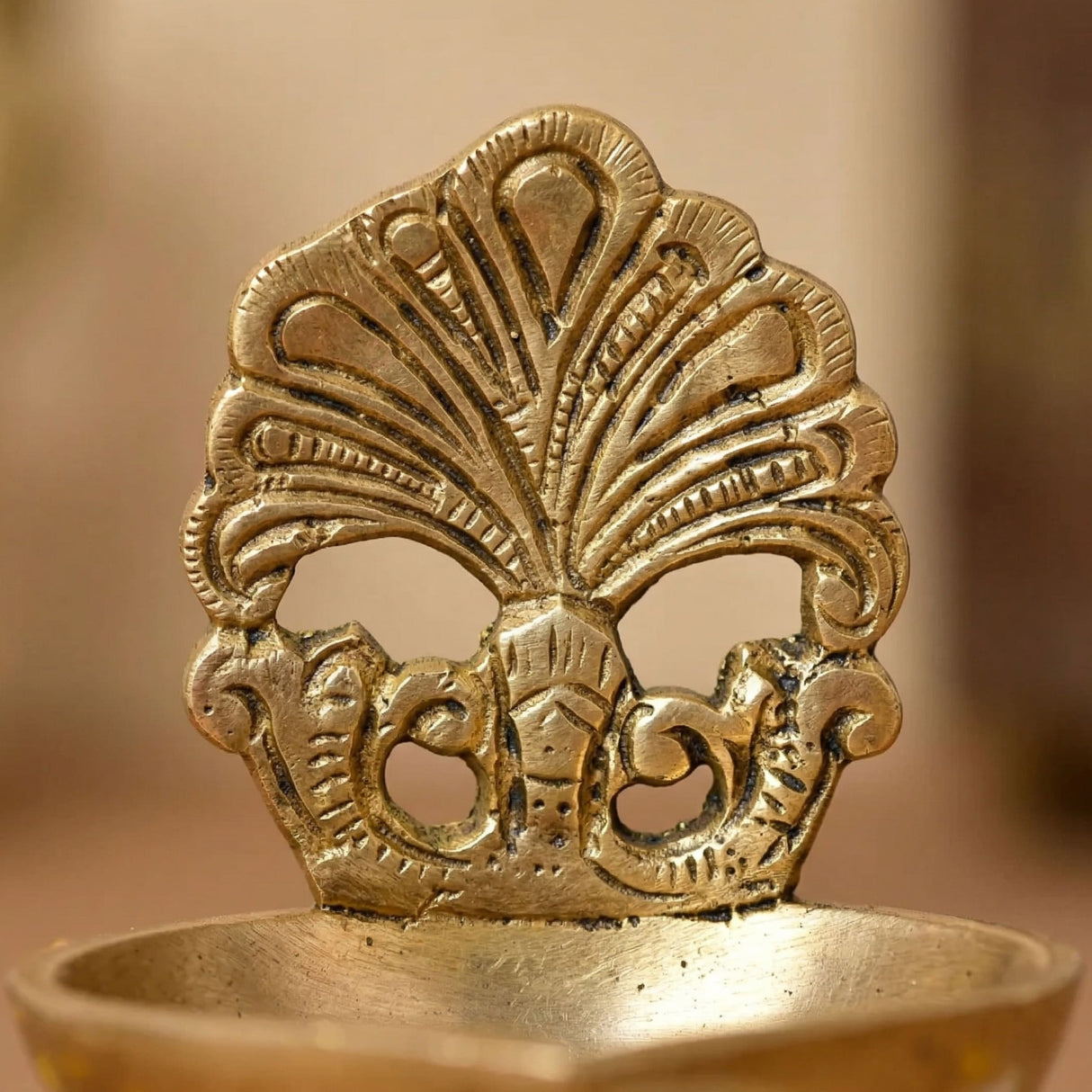 Golden brass diya oil lamp with intricate peacock feather design and ornate base for traditional Hindu puja and home decor