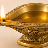 Golden brass diya oil lamp with intricate engraved patterns and lit wick for traditional hindu puja and home decoration