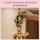 Golden brass ganesha wall hanging diya suspended above a lit multi-flame oil lamp for home temple diwali decor