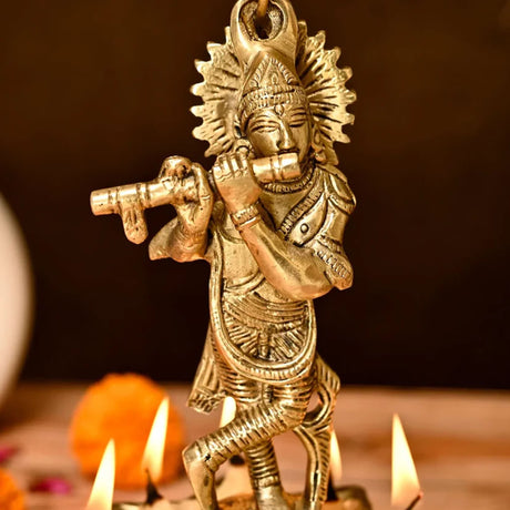 Golden brass figurine of hindu deity krishna playing flute with diya bells chain for home temple diwali decor