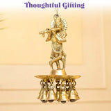 Golden brass figurine of lord krishna playing flute mounted on tiered base with five hanging bells for diya lamp decor