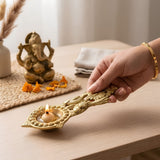 Golden brass diya with intricate peacock and floral designs holding a lit oil lamp for aarti and pooja use