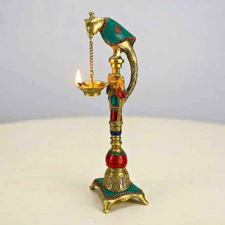 A golden brass elephant oil lamp diya with intricate engravings turquoise and red accents lit wick for temple decor
