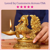 Golden brass peacock diya oil lamp with intricate feather detailing holding lit lamp for diwali and puja decoration