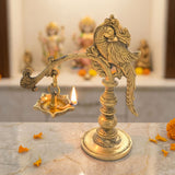 Golden brass peacock-themed annam oil lamp diya with intricate carvings and lit flame for home temple and diwali decoration