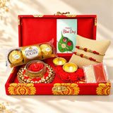 Red and gold brocade bhai dooj gift hamper with ferrero rocher chocolate decorative items and two designer rakhis