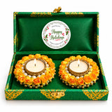 Two golden tealight candle holders decorated with yellow artificial roses and pearls in a green brocade gift box