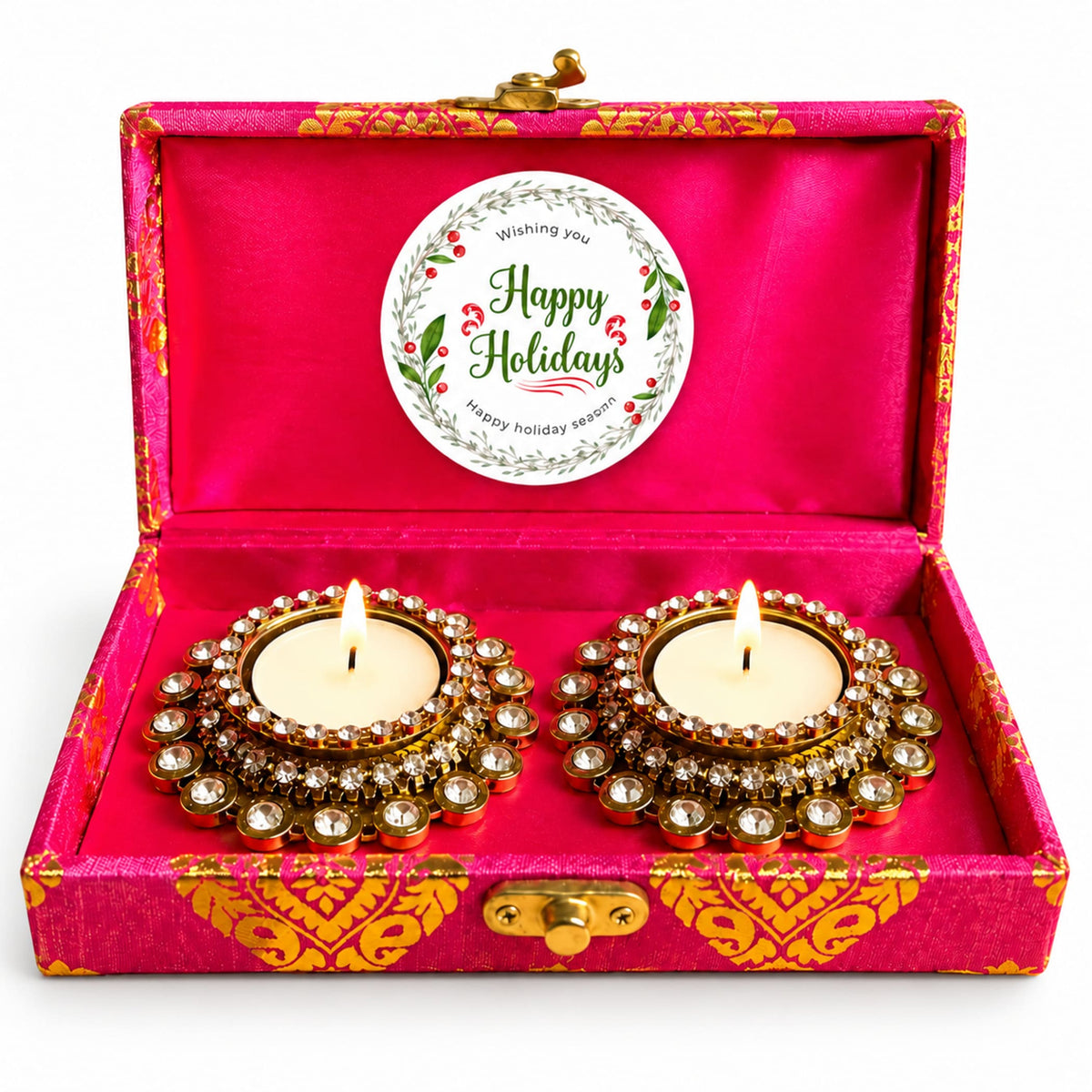 Two gold-plated diya lamps with clear crystals and lit candles in a pink satin box from happy holidays gift hamper