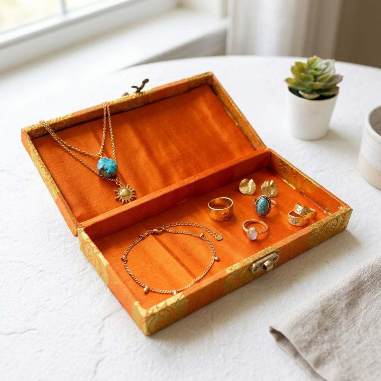 Orangish velvet-lined brocade gift box with gold trim and clasp holding golden jewelry for Indian wedding favors