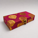 A rectangular magenta brocade fabric gift box with gold damask patterns and a brass clasp for indian weddings