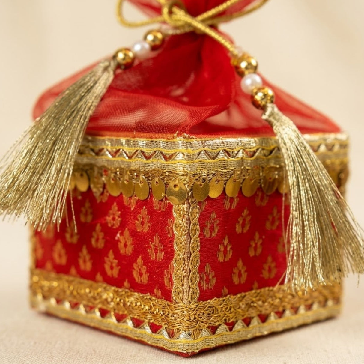 Red and gold embroidered brocade potli gift box with tassels pearls and metallic coins for traditional indian weddings