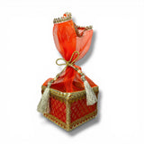 A vibrant red brocade potli gift box with gold trim tassels and organza top for traditional indian wedding favors