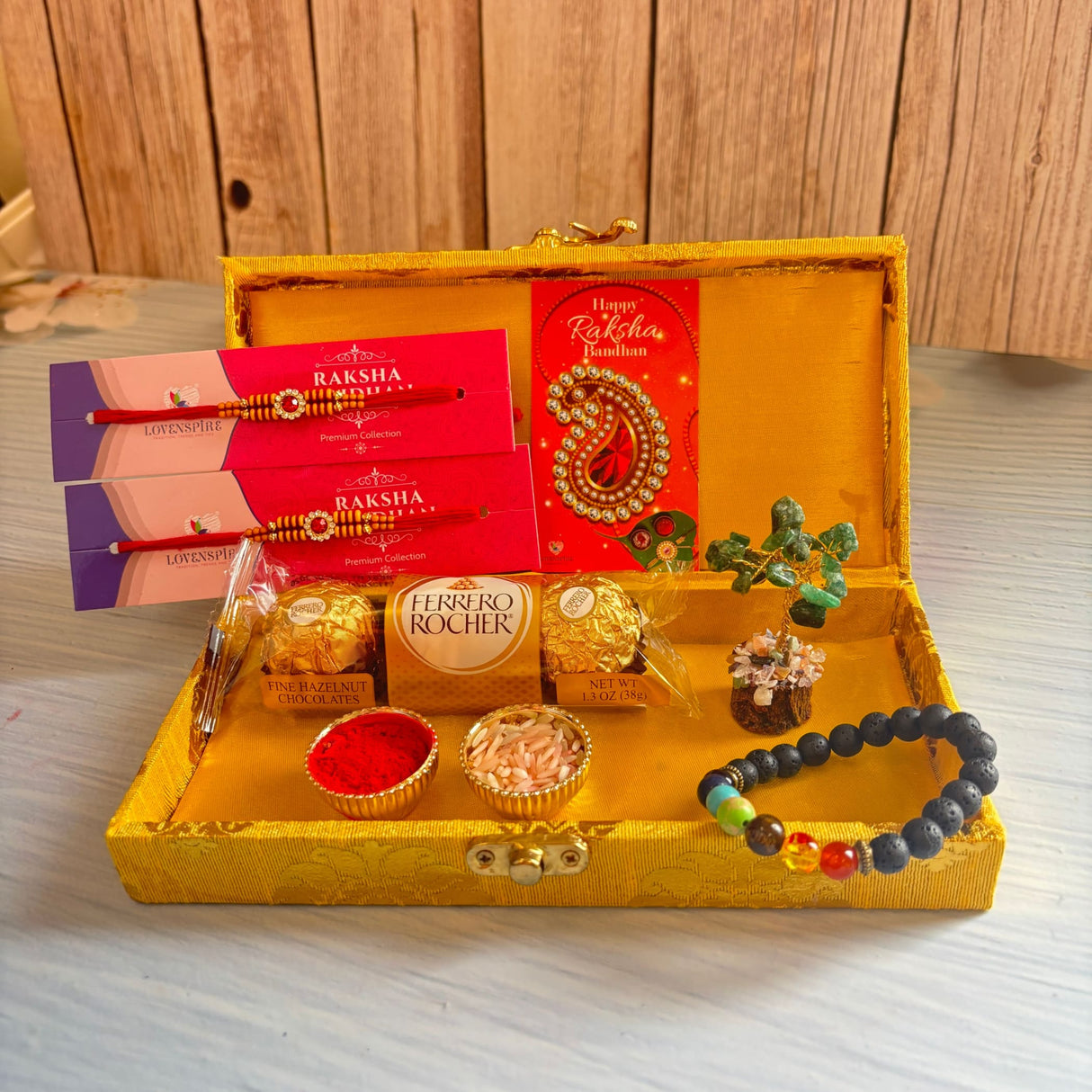 Designer rakhi gift hamper with golden ornate box containing red and gold rakhis, chakra bracelet, chocolates, and roli chawal