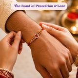 A red thread rakhi with golden beads and a central red gemstone from the designer rakhi gift hamper for brother bhabhi