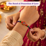Designer rakhi gift hamper set featuring a vibrant red green and blue rakhi bracelet with gold plated gemstone charm