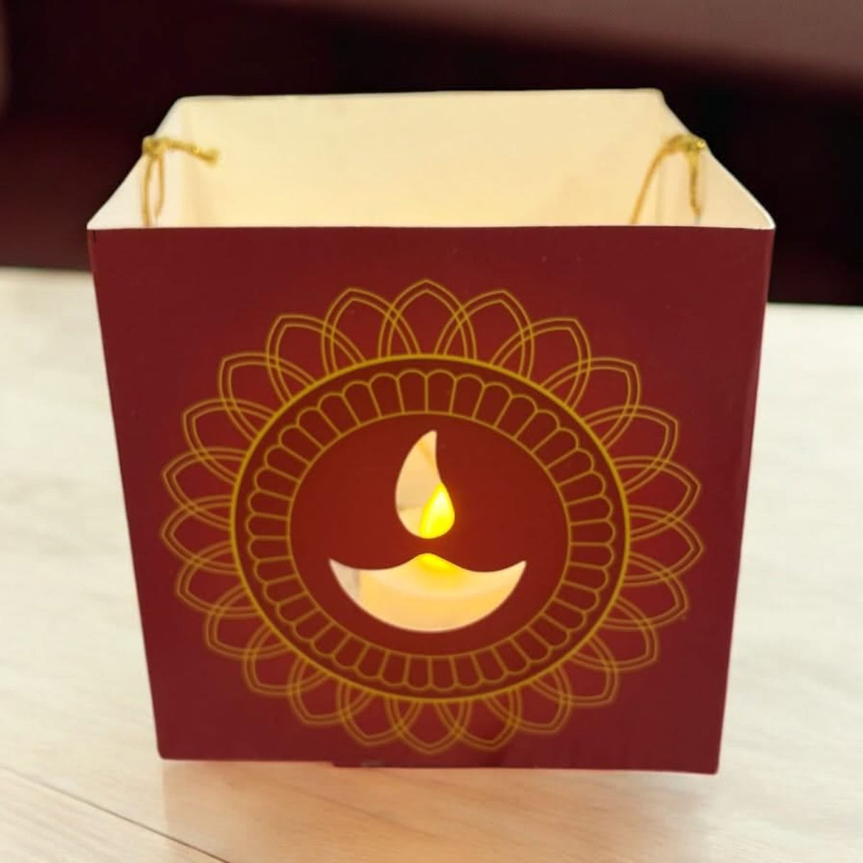 Maroon paper lantern with golden mandala design and lit diya cutout for Diwali decoration