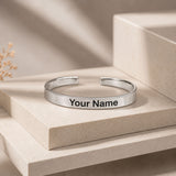 A sleek silver-toned metal cuff bracelet with minimalist design and engraved your name on the inner surface