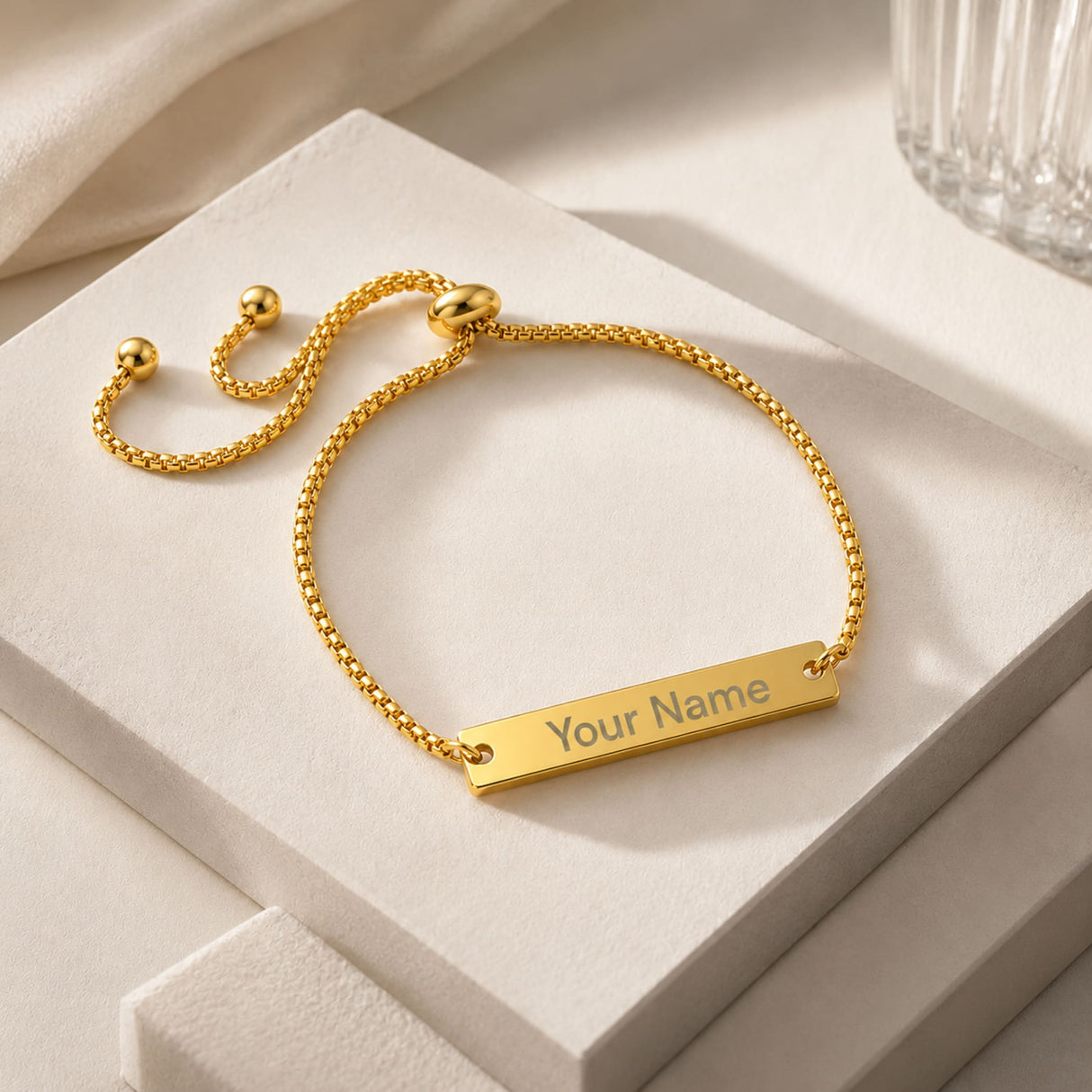 Gold-colored adjustable bracelet with engraved rectangular metal nameplate connected by a minimalist box chain