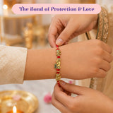 A red and gold rakhi bracelet with intricate elephant charms beadwork and a bro charm in a traditional gift set for brother